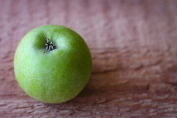 Green apple stands on an unprocessed wooden board