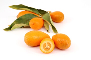 Kumquat fruits , Citrus japonica is the scientific name, on white background with their leaves.  One of them is cut in half.