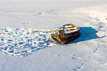 Wooden old boat in a frozen river or lake in a evening winter.