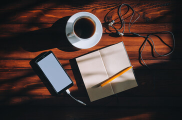 Black smartphone with white screen, paper notebook, pen, headphone and cup of coffee lies on a...