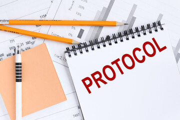 Protocol. text on a white notepad on a light background next to financial charts and a sticker.