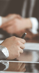 Obraz premium Unknown businessman shaking hands with his colleague or partner above the glass desk in modern office, close-up. Business people group at meeting