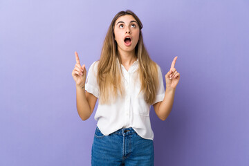 Young woman over isolated purple background surprised and pointing up