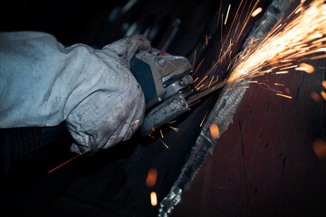 The worker is grinding metal with an angle grinder