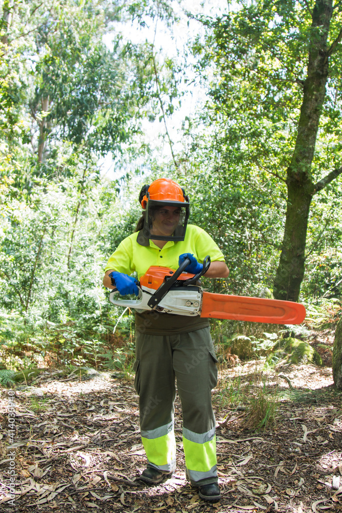 Wall mural female forestry worker or lumberjack using chainsaw to cut trees in forest