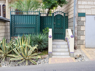 A dark turquoise decorative fence with a wicket gate with marble steps and an agave growing in...