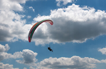 Two seated paraglider flying is cloudy sky