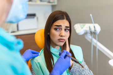Young woman holding cheek in chair at dentist, having toothache. Shot of a young woman suffering...