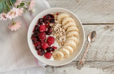 Yogurt bowl with sliced bananas, raspberry and cranberry fruits. Oatmeal with fruits.