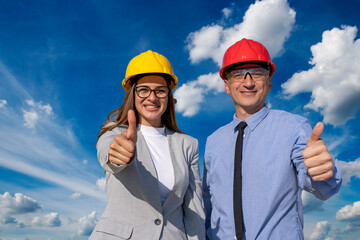 Smiling Man and Woman in Hardhats With Thumbs Up Against Blue Sky With White Clouds