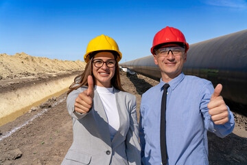 Smiling Man and Woman in Hardhats With Thumbs Up at Gas Pipeline Construction Site