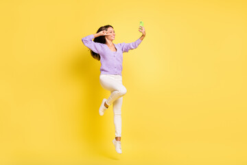 Fototapeta na wymiar Full length body size view of lovely cheerful girl jumping taking selfie showing v-sign isolated over bright yellow color background