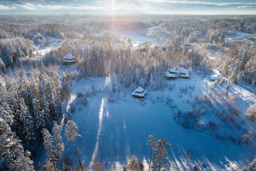 Fototapeta na wymiar Wooden cabins captured from birds eye view, deep winter snow during sunny morning.