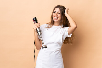 Woman using hand blender over isolated background smiling a lot