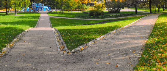 Two wide, straight hiking trails in the park diverge in different directions. The paths are covered...