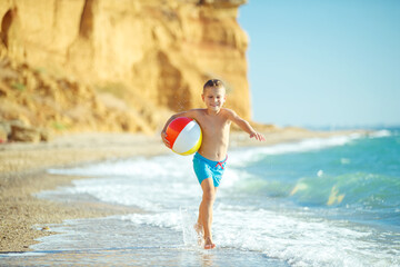 Boy child has fun at sea. Summer, happiness, sea and a child with a ball. High quality photo.