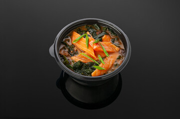 Miso soup with salmon and shitake mushrooms. In a container for delivery. View from above. Dark mirror background.