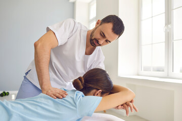 Osteopath in medical uniform fixing woman patients shoulder and back joints in manual therapy clinic