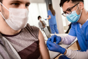 Male nurse with mask giving vaccine to patient in clinic.