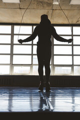 Fototapeta na wymiar Silhouette Athlete man jumping rope in the gym in front of large panoramic windows