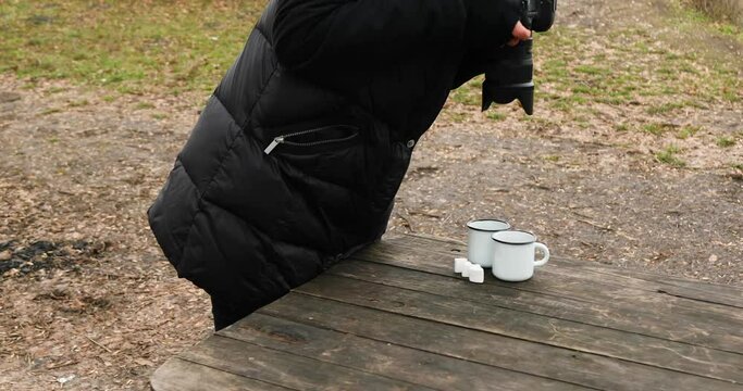 Woman photographer, blogger, travel, hobby and lifestyle concept, female hold in hand camera and take photo from two enamel cups camping tea, outdoor.