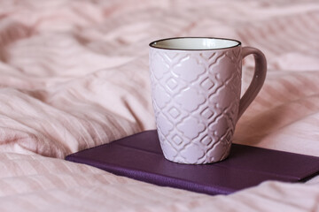 Fototapeta na wymiar A pink cup of tea sits on the pink blanket in the bed.Home atmopshere.
