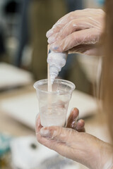 a girl in transparent gloves pours paint from a white bottle into a small transparent glass with resin