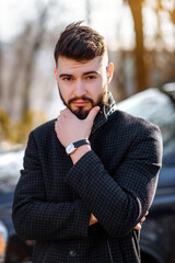 Portrait of bearded stylish young handsome man in black coat outside.