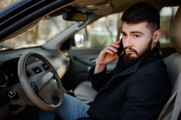bearded stylish young handsome man in black coat sitting in the car