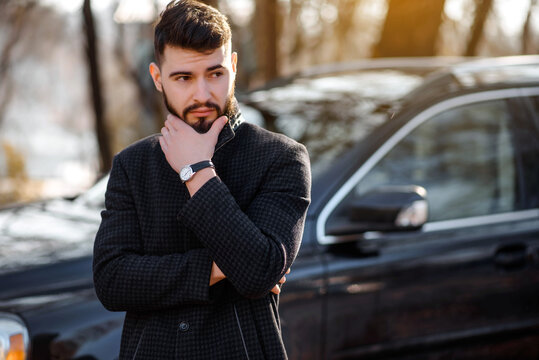 Portrait of bearded stylish young handsome man in black coat outside.