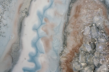 a beautiful splash of transparent stones and silver powder on streams of color powder, white, silver and delicate blue resin, blurred waves. imitation of precious stones on an abstract background
