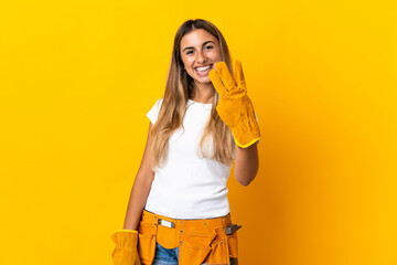 Young hispanic electrician woman over isolated yellow wall happy and counting three with fingers
