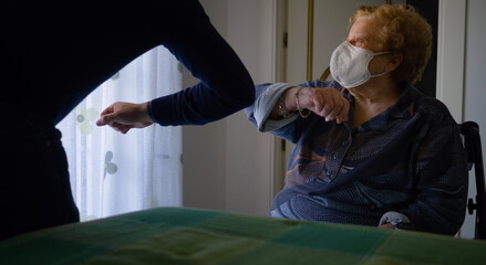 An elderly woman and a young man greet each other with an elbow bump while wearing an ffp2 mask.