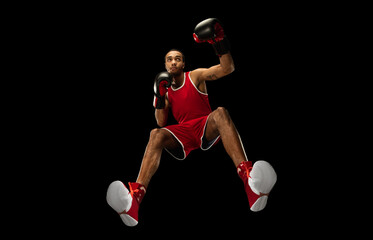 Young african-american professional boxer in action, motion isolated on black background, look from the bottom. Concept of sport, movement, energy and dynamic, healthy lifestyle. Training, practicing.
