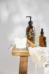 White scented candle, body lotion, essential oils and delicate flowers on wooden bench