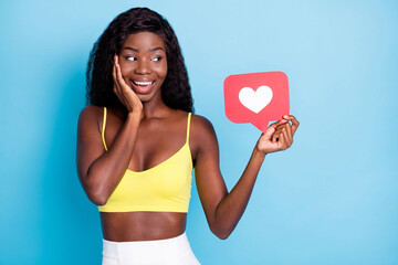 Photo of pretty impressed dark skin curly girl dressed yellow singlet holding red like card isolated blue color background