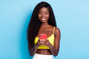 Photo cute pretty dark skin curly girl dressed yellow singlet holding modern device isolated blue color background