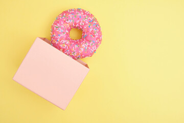 donut with sprinkles and pink icing in a gift box on a yellow background