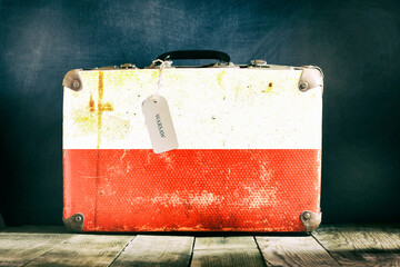 Old suitcase with the Poland flag on wooden background.