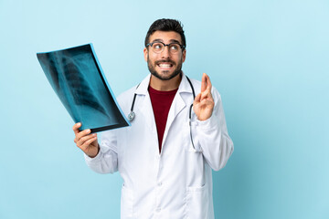 Professional traumatologist holding radiography isolated on blue background with fingers crossing