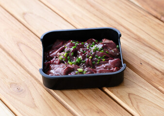 fresh raw offal sliced on square plate isolated on wooden background, shabu, hot pot ingredients