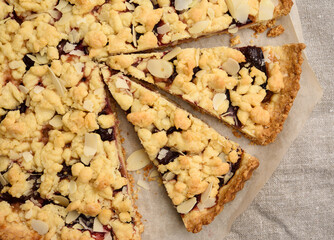 baked round crumble pie with plum cut into pieces on a black background