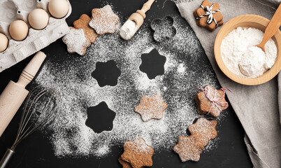 Star shaped baked gingerbread cookies sprinkled with powdered sugar on a black table