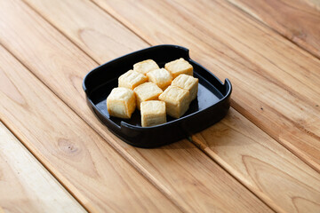 fresh raw tofu sliced on square plate isolated on wooden background, shabu, hot pot ingredients