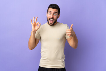 Young handsome man with beard over isolated background showing ok sign and thumb up gesture