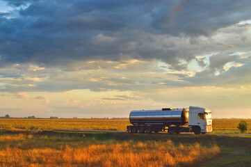 Truck driving on a road at sunset. Beautiful early evening cloudy sky. Sunlit grass in the foreground