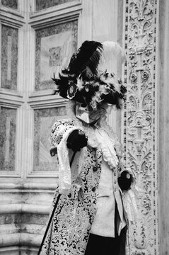 Mask in  in traditional Venetian costume perfectly compatible with palazzo wall at background at traditional Carnival in Vemice, Italy. Black white historic photo.
