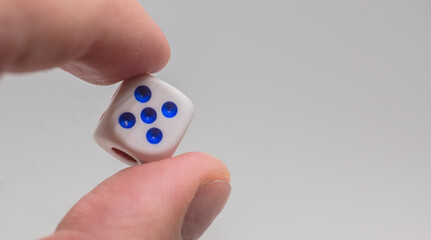 One dice with number four in hand. White dice on white background. Concept of luck, chance and leisure fun.