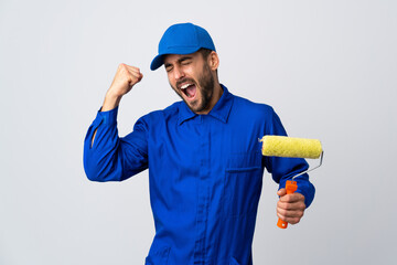 Painter man holding a paint roller isolated on white background celebrating a victory