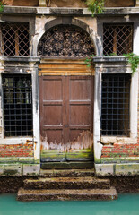 Fototapeta na wymiar Abandoned palazzo at a Venetian canal. Smashed windows (no glass), rusty bars, empty interior.